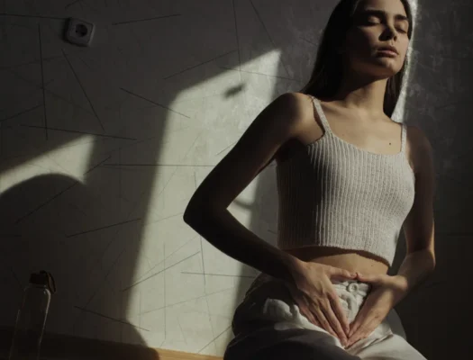 A woman sitting on the floor with her hands resting on her stomach, focusing on her pelvic floor health.