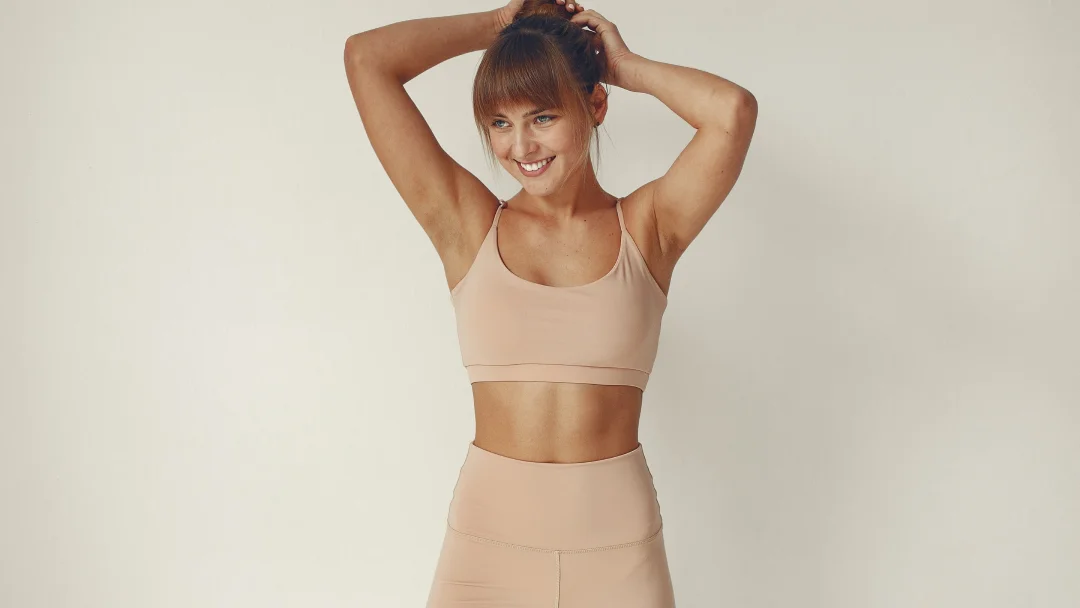 Femme en brassière sportive beige et short, posant avec confiance, symbolisant la perte de graisse et le bien-être.