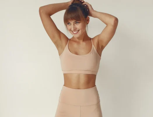 A woman wearing a tan sports bra and shorts, showcasing her fitness journey and dedication to fat loss.