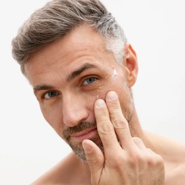 A shirtless man with a beard touches his face, preparing for a neuromodulator injection.