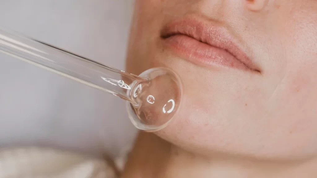 A woman receives a facial treatment, applying a facial brush after a hyaluronic acid injection.