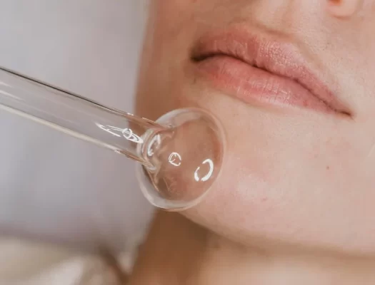 A woman receives a facial treatment, applying a facial brush after a hyaluronic acid injection.