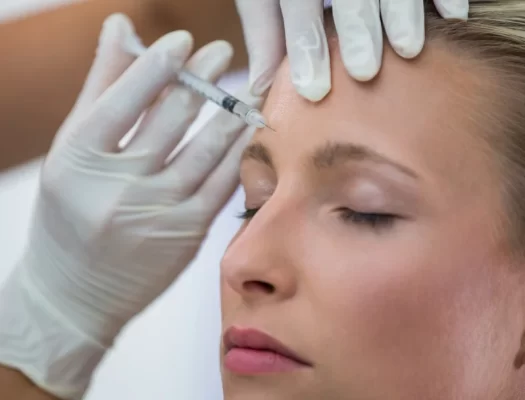 A woman receiving a neuromodulator injection in her forehead at a medical clinic.