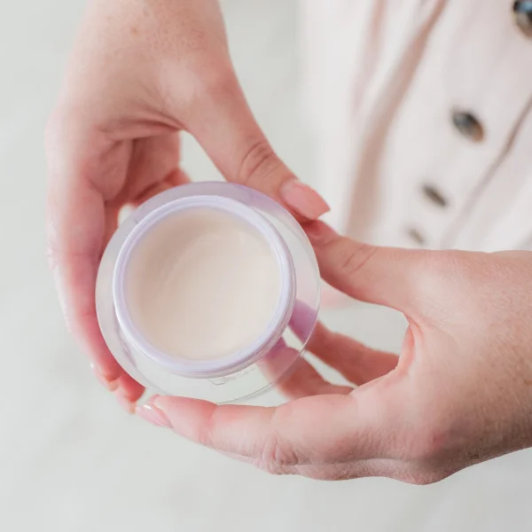 A person holding a small container of cream, demonstrating a skincare routine for firming facial skin.