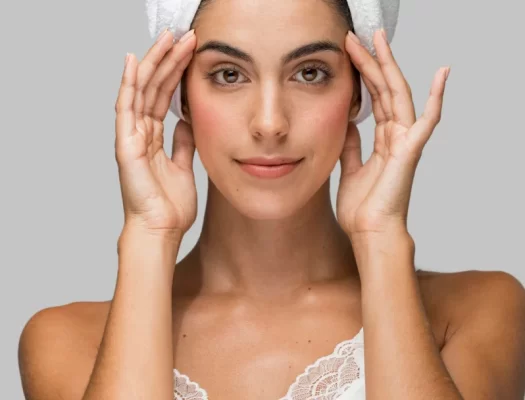 A woman with a towel on her head, demonstrating a skincare routine for firming facial skin.