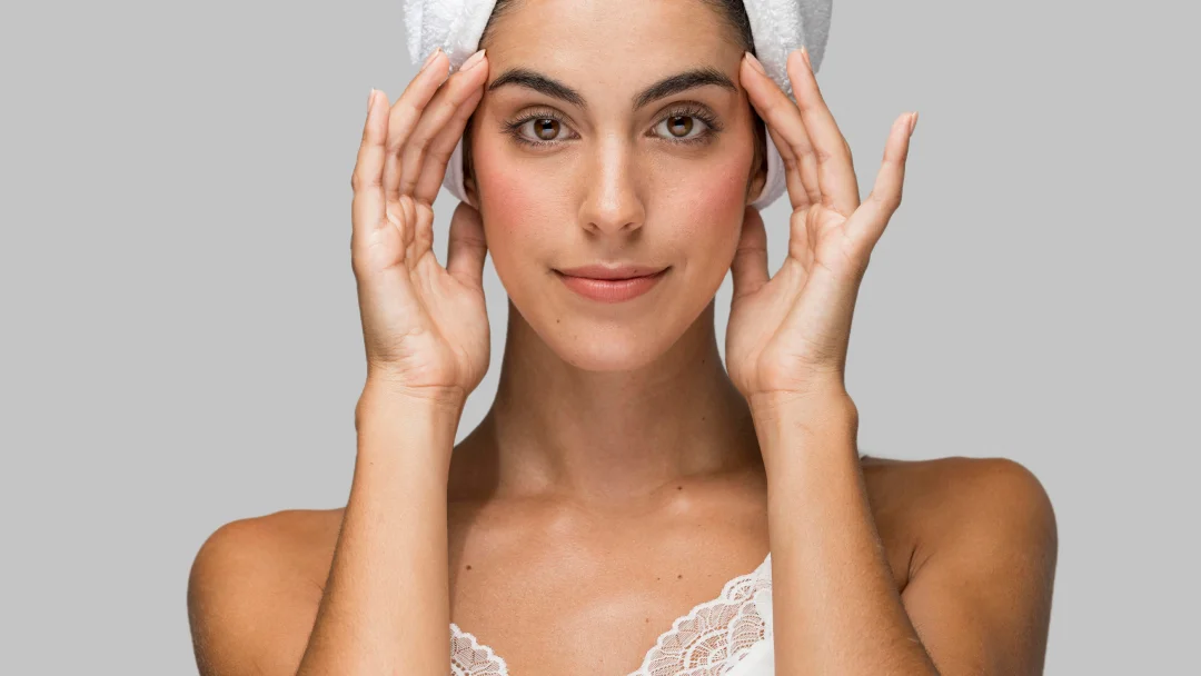 A woman with a towel on her head, demonstrating a skincare routine for firming facial skin.