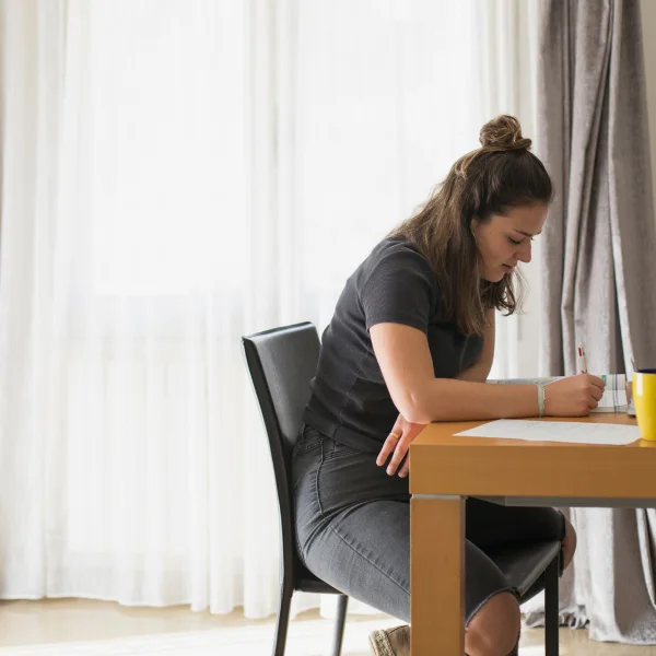A woman sitting at a table, focused on writing notes about losing a double chin.